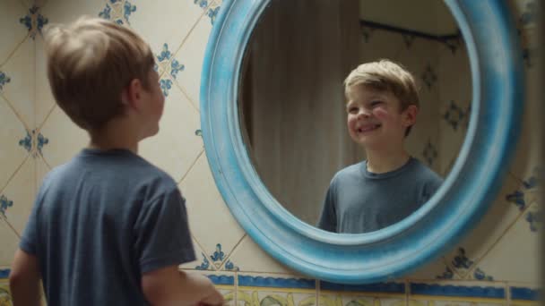 Niño rubio preescolar mostrando la lengua y luego cepillándose los dientes en el baño en casa. Reflejo espejo de niño con cepillo de dientes en las manos haciendo rutina de la mañana — Vídeo de stock