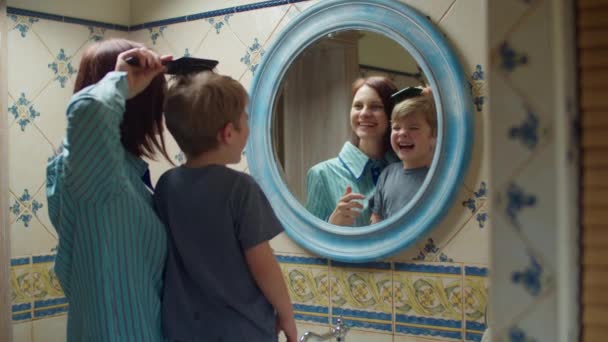 Jonge moeder uit de 30 poetst haar kleuter zoons haar thuis in de badkamer. gelukkig familie maken schoonheid routine in spiegel reflectie. — Stockvideo