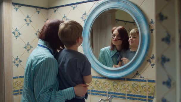 Joven madre de 30 años con hijo preescolar divirtiéndose en el baño en casa. Familia feliz abrazándose y riendo juntos en el reflejo del espejo . — Vídeo de stock