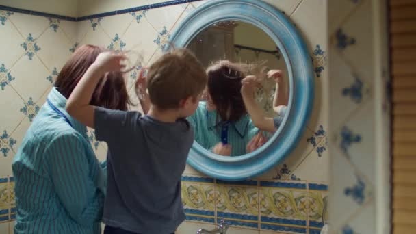 Молодая 30-летняя мать с дошкольным сыном развлекаются с водой в ванной комнате дома. Счастливая семья смеется и играет с водой вместе в зеркальном отражении . — стоковое видео