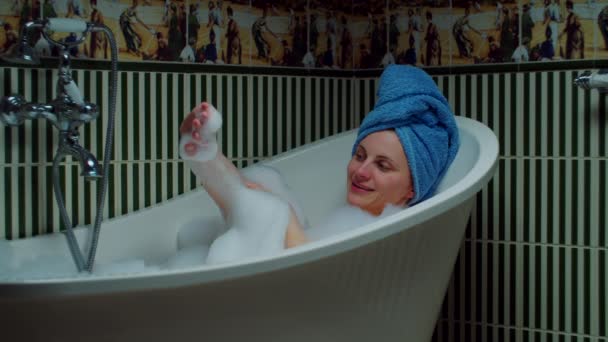 Jeune femme des années 30 prenant un bain et jouant avec de la mousse dans la salle de bain verte à la maison. Femme avec serviette bleue sur la tête relaxant dans la baignoire . — Video