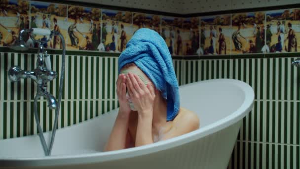 Junge Frau in den 30er Jahren wäscht Gesichtsmaske in Badewanne mit Schaum im grünen Badezimmer zu Hause ab. Frau mit Handtuch auf dem Kopf macht Badeverfahren. Nahaufnahme — Stockvideo