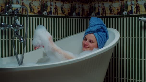 Mujer joven de 30 años tomando baño y jugando con espuma en el baño verde en casa. Mujer con toalla azul en la cabeza relajante en la bañera . — Vídeos de Stock