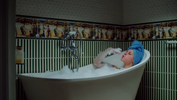 Jeune femme des années 30 prenant un bain et jouant avec de la mousse dans la salle de bain verte à la maison. Femme avec serviette bleue sur la tête relaxant dans la baignoire . — Video