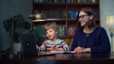 Anaokulu çocuğu evde 30 'lu yaşlardaki genç annesiyle online ödev yapıyor. Bilgisayarda el sallayarak öğretmenini selamlayan bir çocuk. Çevrimiçi eğitim süreci. 