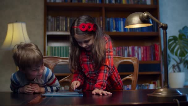 Två förskolebarn spelar spel på surfplatta hemma. Syskon skrattar tillsammans med hjälp av program på gadget. Glad pojke och flicka spelar online. — Stockvideo