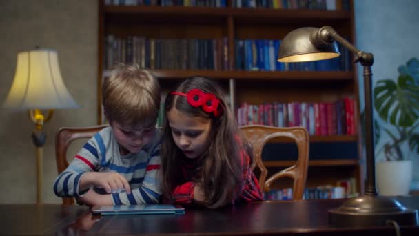 两个学龄前儿童在家里的平板电脑上玩游戏。在小工具上使用应用程序时，兄弟姐妹们一起大笑。快乐的男孩和女孩在网上玩. — 图库视频影像