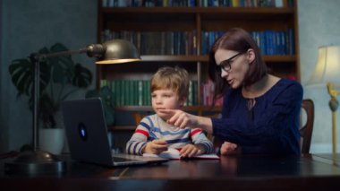 Anaokulu çocuğu evde 30 'lu yaşlardaki genç annesiyle online ödev yapıyor. Çocuk egzersiz defterine yazıyor. Çevrimiçi eğitim süreci. 
