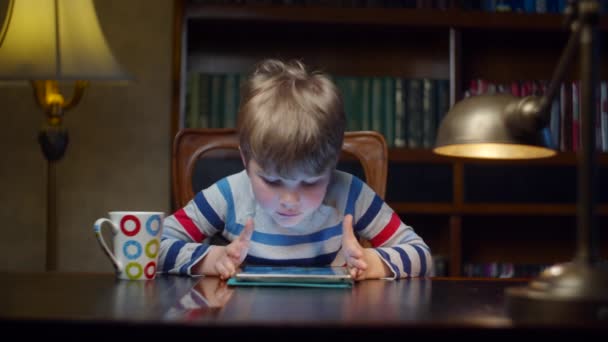 Niño de la escuela jugando juegos en la tableta y beber agua en casa. Niño usando aplicación en línea en gadget sentado en el escritorio con lámpara en cámara lenta . — Vídeo de stock