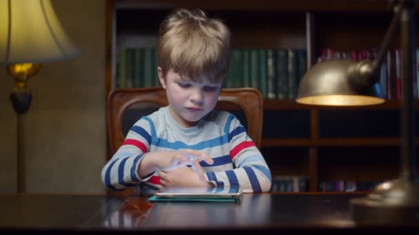 Okullu çocuk evdeki tablet bilgisayarda oyun oynuyor. Çocuk internet uygulamasını cihazda kullanıyor. Masasında lamba ile ağır çekimde oturuyor.. — Stok video