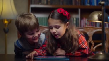 Evde tablet bilgisayarda oyun oynayan iki anaokulu çocuğu. Kardeşler birlikte gülüyor. Alet üzerinde başvuru yapıyorlar. Mutlu çocuk ve kız internette oynuyor.. 