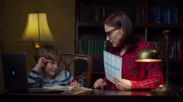 Menino pré-escolar fazendo trabalhos de casa de matemática com a jovem mãe de 30 anos em casa. Miúdo a olhar para equações matemáticas e a escrever no caderno. Processo de ensino em casa . — Vídeo de Stock