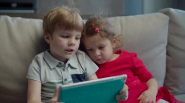 Anaokulu çocuğu ve kız evdeki kanepede oturan tablet bilgisayar kullanıyorlar. Çocuklar tablet bilgisayarda mobil uygulama kullanıyorlar.. 