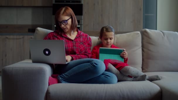Устал работать из дома 30-х женщина закрывая ноутбук с маленькой дочерью, используя планшетный компьютер, сидя на диване дома. Семья использует гаджеты дома. Онлайн работа и обучение . — стоковое видео