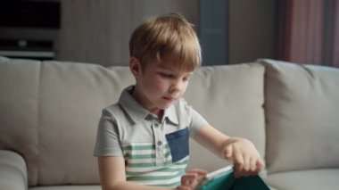Anaokulu çocuğu evdeki kanepede otururken online eğitim için tablet bilgisayar kullanıyor. Çocuk internetten okumak için başvuru kullanıyor. Aleti olan çocuk.