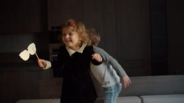 İki anaokulu çocuğu karanlık odadaki kanepede zıplayıp gülüyor. Sevimli küçük kız, kardeşiyle kanepede ağır çekimde eğleniyor.