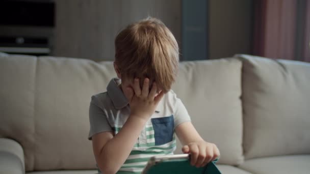 Niño preescolar usando tableta de computadora para la educación en línea sentado en el sofá en casa. Niño usando la aplicación para estudiar en línea. Niño con gadget. — Vídeo de stock