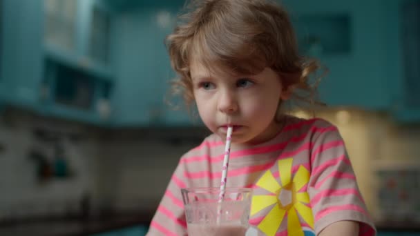 Linda niña en camiseta rosa bebiendo batido de bayas con paja de papel en casa cocina azul. Los niños disfrutan del batido casero. De cerca. — Vídeos de Stock