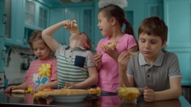 Evdeki mavi mutfakta ev yapımı pizza ve patates yiyen dört melez çocuk grubu. İki erkek ve iki kız elleriyle pizza yemekten hoşlanırlar..