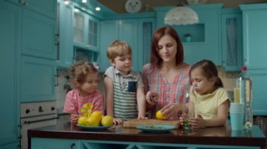 Üç çocuklu bir aile ev yapımı limonata, nane ve soda yapıyor. Genç anne, mavi mutfakta çocuklarla yemek pişiriyor.
