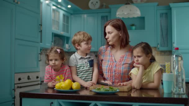 Familie mit drei Kindern macht hausgemachte Limonade aus Zitronen, Minze und Limonade. Junge Mutter kocht mit Kindern in blauer Küche zu Hause — Stockvideo