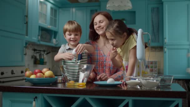 Feliz familia de madre y dos hijos cocinando tarta de manzana junto con huevos, azúcar, harina y manzanas. Chico rompiendo huevo en tazón de vidrio . — Vídeos de Stock