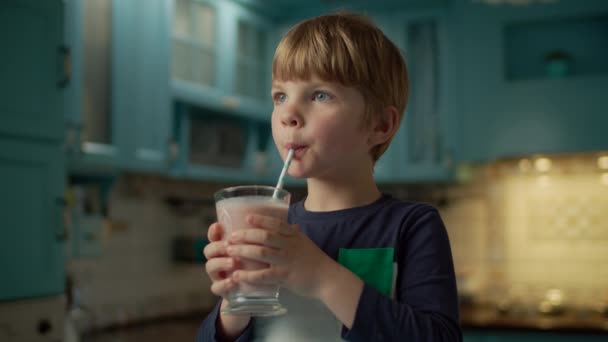 Retrato de menino pré-escolar loiro gosta de beber smoothie de frutas de pé na cozinha azul. Criança bebendo coquetel de frutas em casa . — Vídeo de Stock