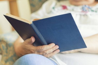 Yaşlı kadın evde kitap okuyor.