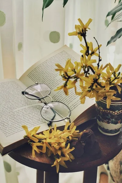 Dark mystic and calm mood. Book and yellow flowers with green leaf on the table, spring morning at home. Time spending while isolated and quarantined. Soft colors. Read and be smart. Education, hobby.