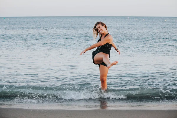 Blonde lachende vrouw uitspatten van water op het strand. — Stockfoto