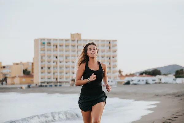 Блондинка бегает по пляжу в черной спортивной одежде . Стоковое Изображение