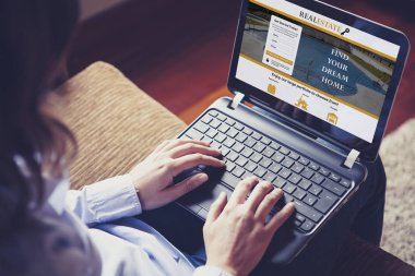 Kadın kanepede otururken bir dizüstü bilgisayar ile bir emlak web sitesi ev arıyorum.