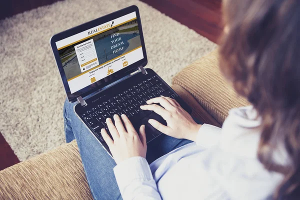Γυναίκα χρησιμοποιώντας ένα φορητό υπολογιστή για να ψάξουν για ένα σπίτι σε μια πραγματική ιστοσελίδα περιουσία, ενώ κάθεται στο σπίτι. — Φωτογραφία Αρχείου