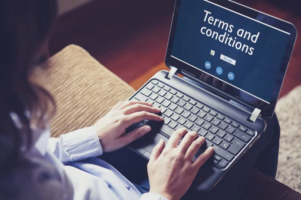 Frau liest Geschäftsbedingungen im Laptop, während sie zu Hause auf dem Sofa sitzt. — Stockfoto