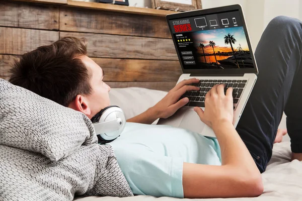 Hombre viendo series de streaming en un ordenador portátil, acostado en el —  Fotos de Stock