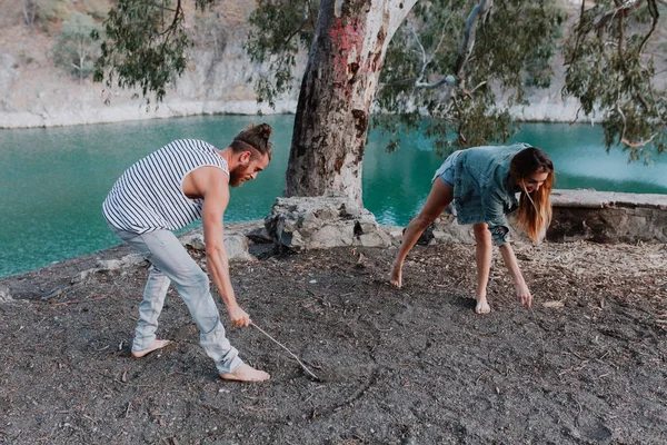 Happy couple drawing shapes on the ground with a stick for fun in nature. — Stock Photo, Image