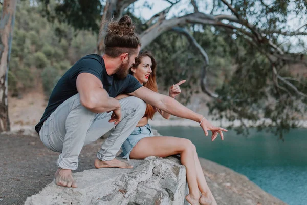 Jeune couple assis près de la rivière contemplant la nature et pointant quelque part — Photo
