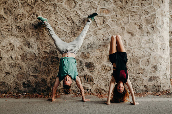 Smiling young couple doing a handstand position in a stone wall Royalty Free Stock Images