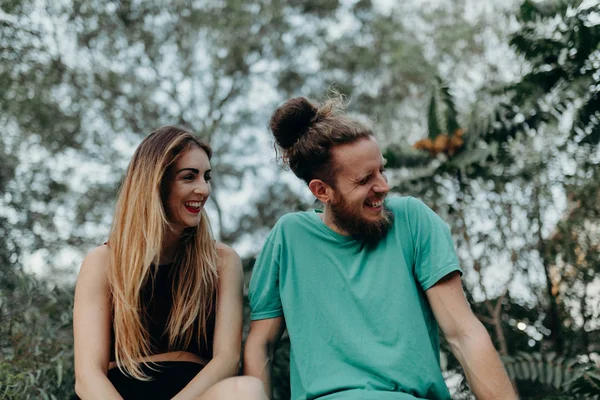 Щаслива альтернативна пара сміється разом, сидячи в природі — стокове фото