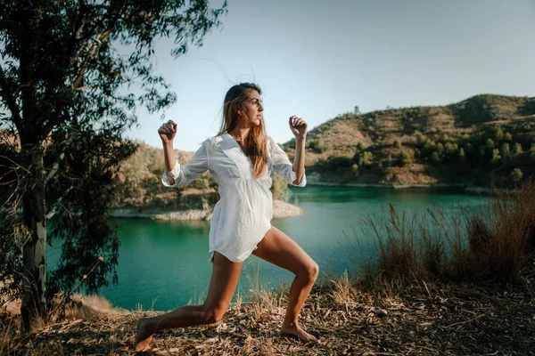 Mujer de camisa blanca bailando en la naturaleza con un lago al fondo — Foto de Stock