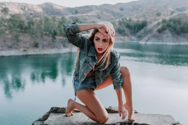 Vrouw in korte broek en jas poseren in de natuur met een meer op de achtergrond — Stockfoto