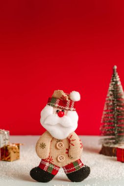 Sevimli Noel baba bebek hediye kazık ve bir Noel ağacı arasında kar yağışı sırasında hissettim. Kırmızı bir arka plan ve güzel ışık.