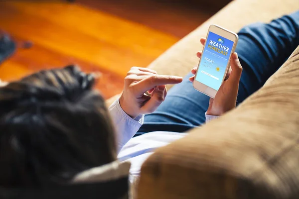 Mujer consultando pronóstico del tiempo en un teléfono móvil en casa . — Foto de Stock