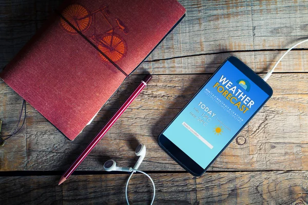 Weather forecast mobile app in a phone screen placed over a wooden table