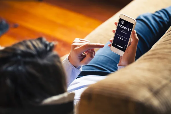 Mujer escuchando podcast en un teléfono móvil mientras se acuesta en un sofá en casa . — Foto de Stock