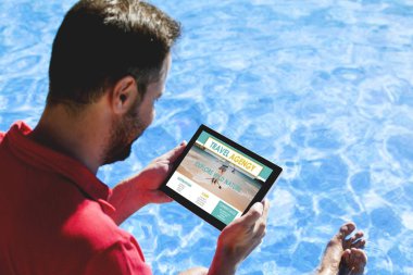 Havuz kenarında otururken bir seyahat acentası Web sitesi bir tablet ile seyahat hedef arayan adam.