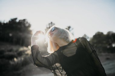 Sevimli sarışın kadın profili güneş gözlüğü ve güneşin arka planda ile poz kavramsal portresi.