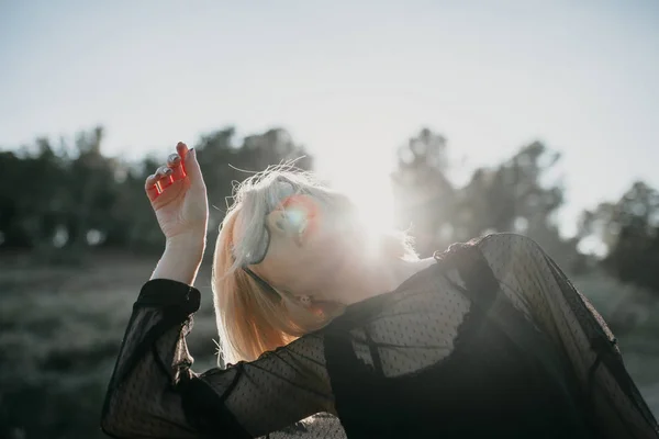 RAD blond meisje dansen en kijken naar de hemel met zonnebril en zwarte kleding. — Stockfoto