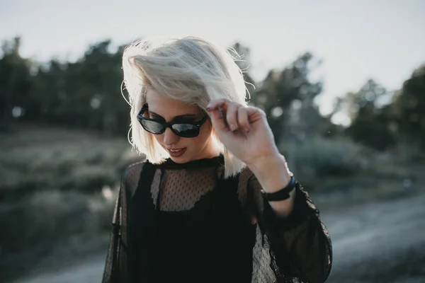 Blond meisje met zonnebril wandelen in de natuur met achtergrondverlichting. — Stockfoto