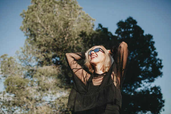 Nette blonde junge Frau mit Sonnenbrille lacht draußen in der Natur. — Stockfoto